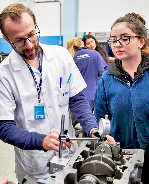 Professor ensinando aluna a mexer em um equipamento