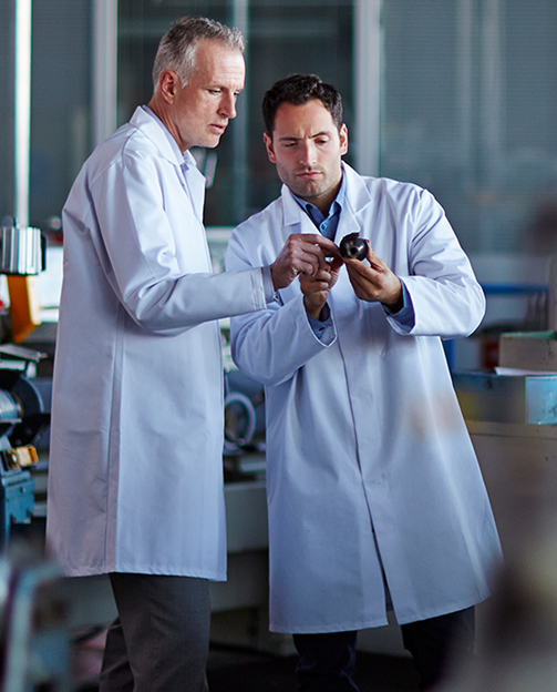Dois homens de jaleco observando um objeto de metal