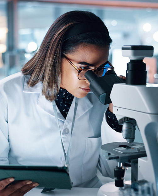 Mulher de óculos usando um microscópio com uma tablet na mão